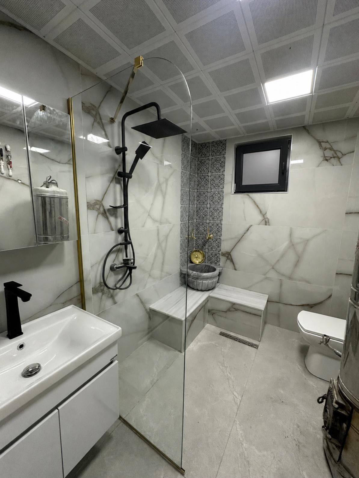 Tadilattan sonra: aynı banyo, mermer desenli seramik, siyah duş seti, kurna ve oturma sekisi