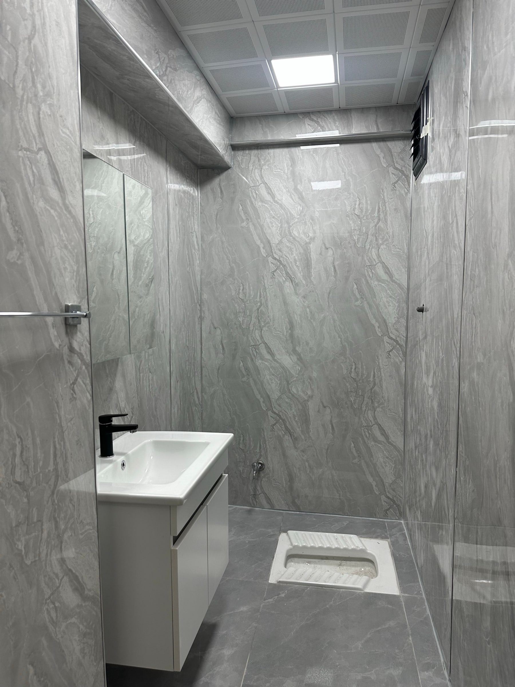 Duvarları gri PVC mermer plaka ile kaplanmış, derzsiz küçük tuvalet